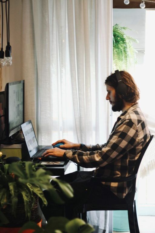 foto ilustrativa do post sobre plantas no home office. Na foto,  homem trabalhando no computador e um vaso de planta em primeiro plano.